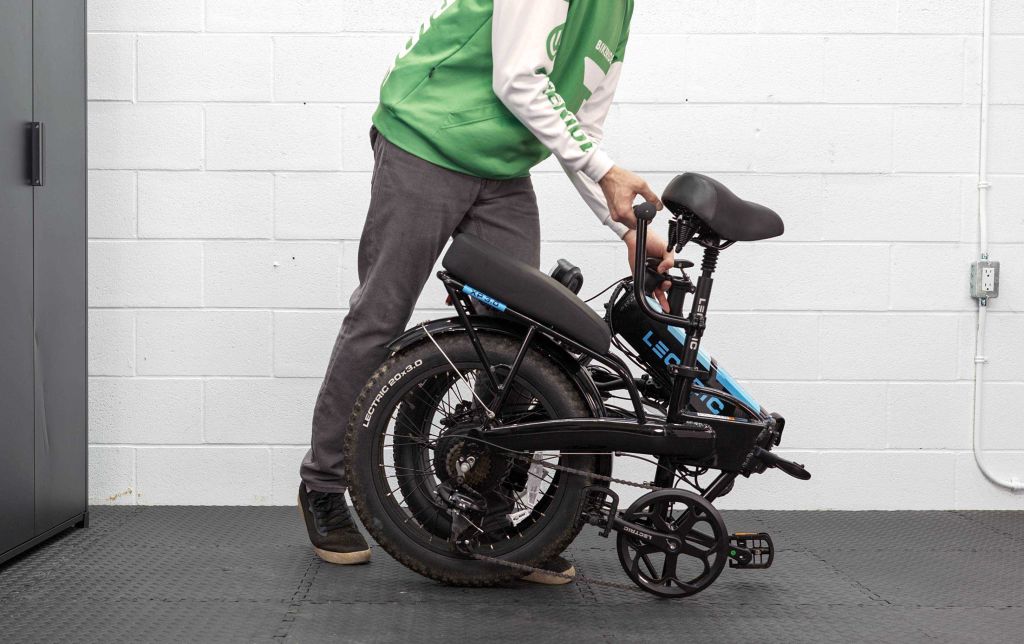 man in a green hoodie folding a bike indoors