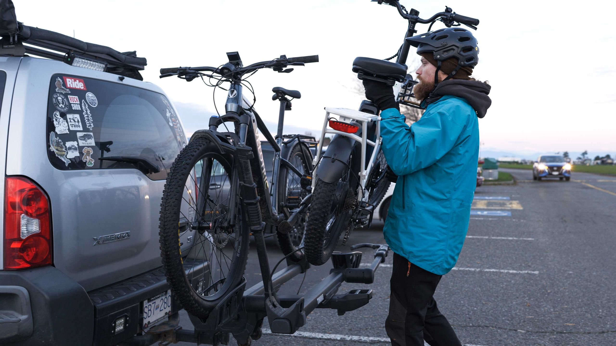 Man in a blue coat loading two bikes onto a platform hitch rack