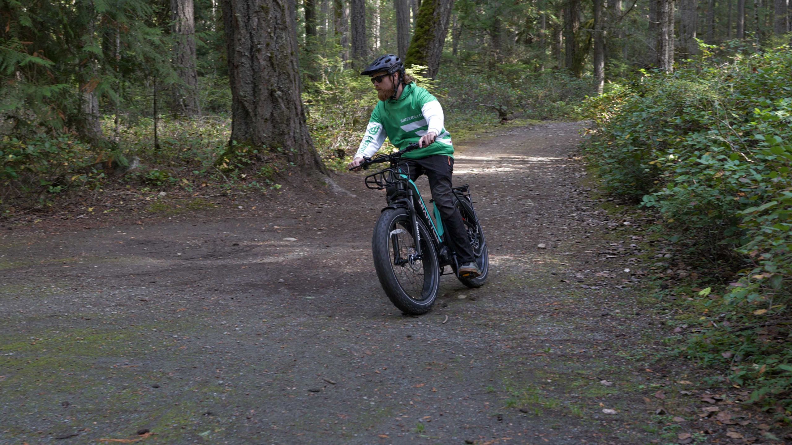 man in a green hoodie riding an ebike on a forrest trail