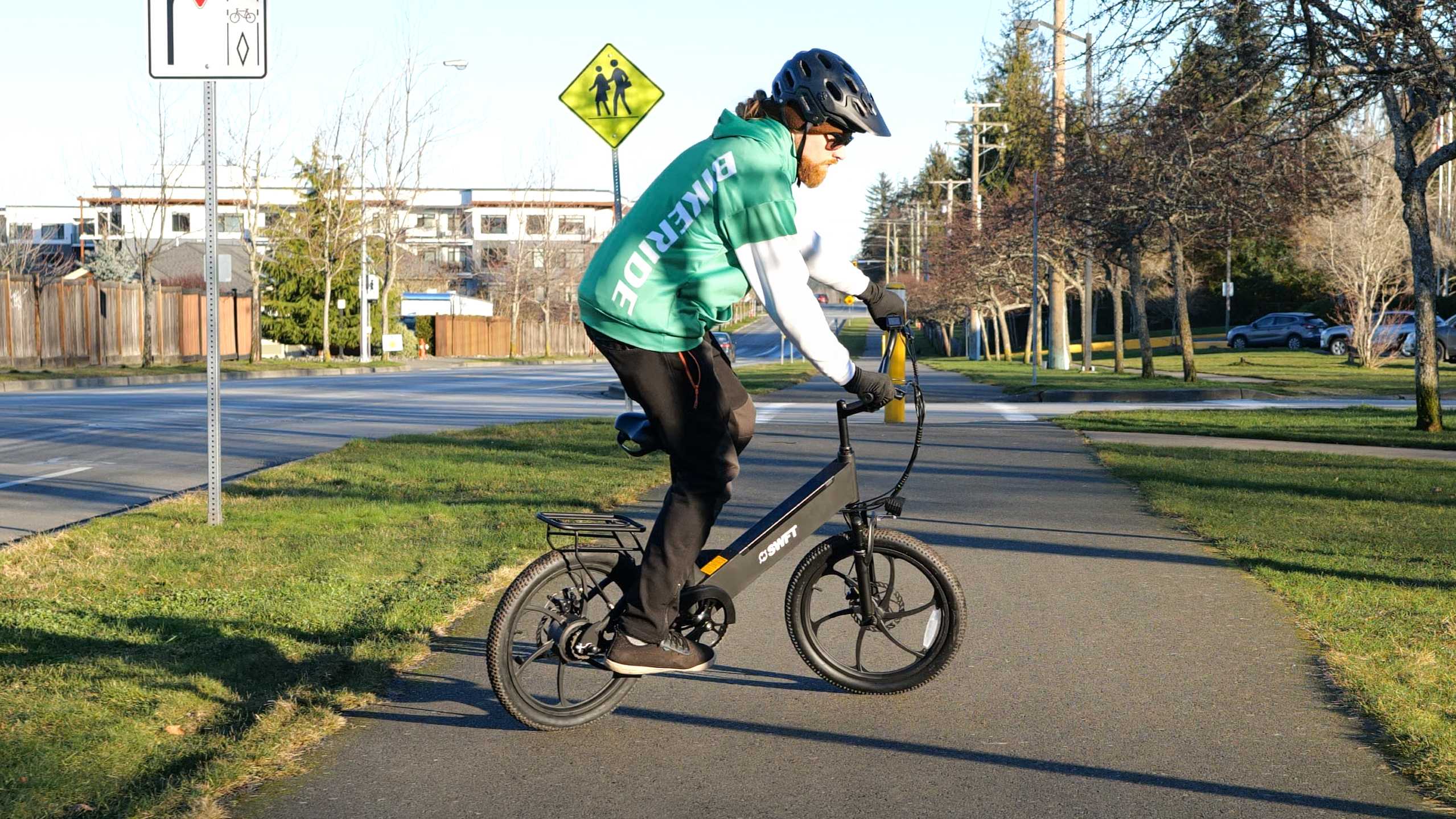 A man wearing a green hoodie riding an e-bike in an urban area